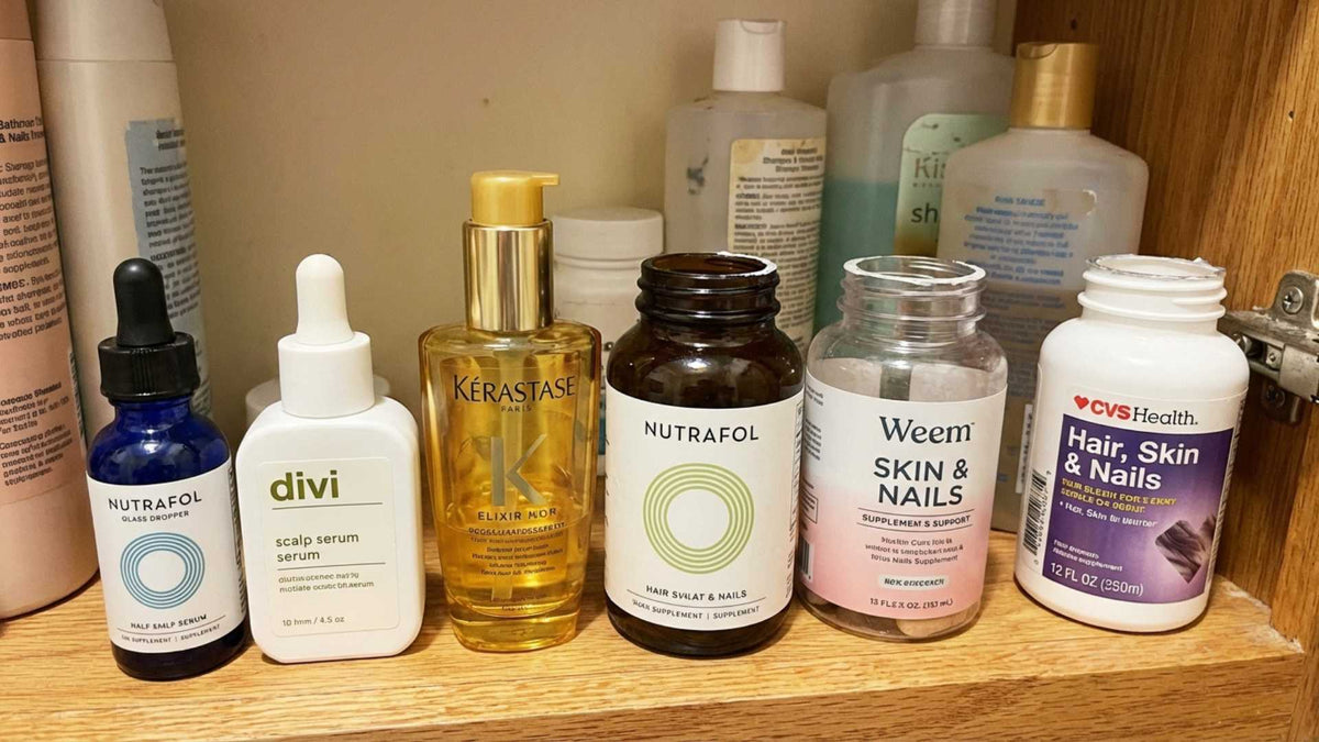 A bathroom shelf with multiple half-used hair products — serums, supplements, shampoos — the evidence of a woman who tried everything
