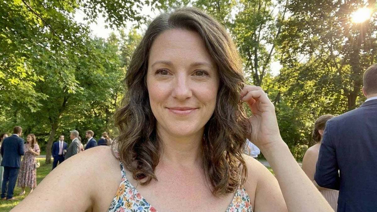 A woman in her early 50s at a casual outdoor gathering, hair down, smiling naturally — looking relaxed and present