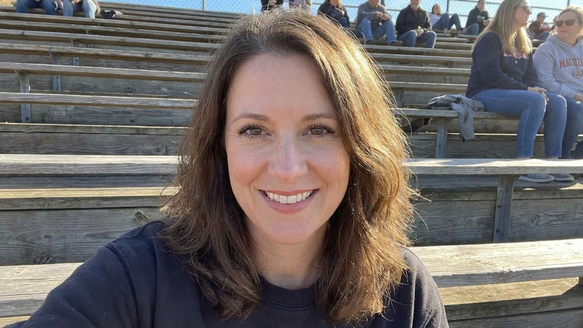 A woman in her early 50s at a casual outdoor gathering, hair down, smiling naturally — looking relaxed and present